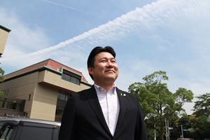一筋の飛行機雲のある青空を背景に、上を見ている長野市長を見上げるように写した写真。