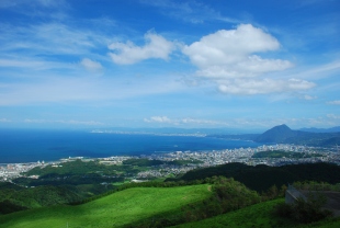 青空を背景にして、山の上から別府市街と別府湾を一望する風景の写真
